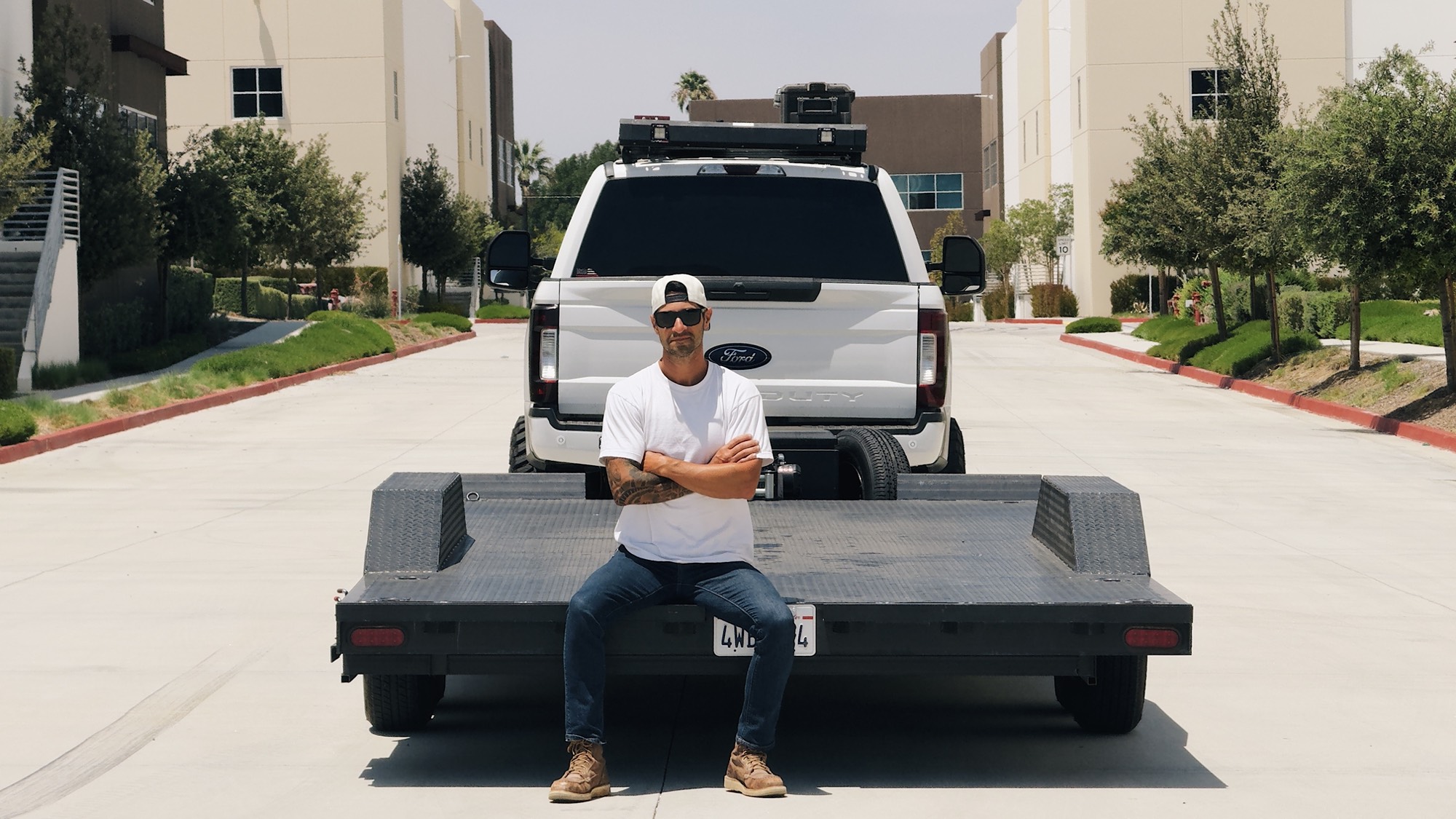 Owner of 412 Trailer Renting seated on the trailer deck with the tow truck behind